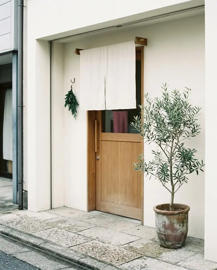 のれんのかかった小さなサロンの入口と鉢植えのオリーブ